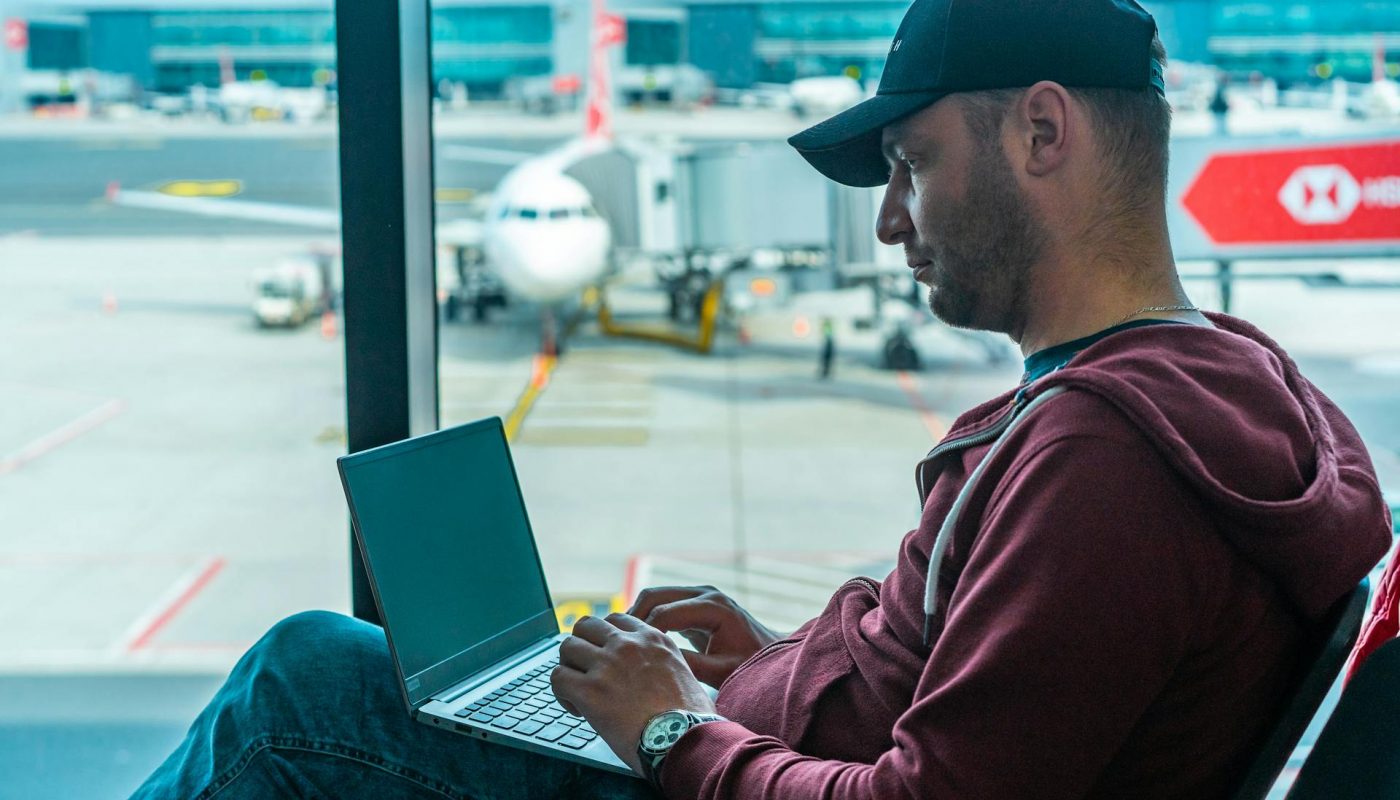 homme avec casquette dans aeroport avec ordinateur sur ses genoux