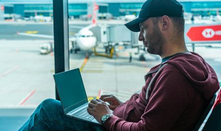 homme avec casquette dans aeroport avec ordinateur sur ses genoux
